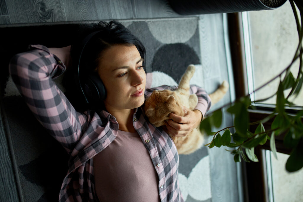 woman relaxing on floor with a playful cat by a sunny window sill